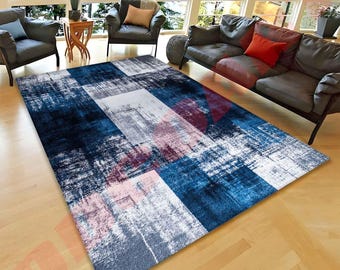 May include: A rectangular rug with an abstract design in shades of blue, white, and grey, with burgundy accents. The rug's pattern consists of overlapping rectangles. It is placed on a light-coloured wooden floor in a living room.