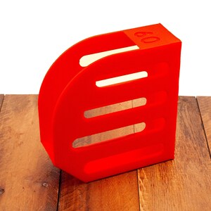 Puede incluir: Un portarevistas de pl&aacute;stico rojo con el n&uacute;mero "09" impreso en el lateral. El portarevistas tiene tres ranuras para revistas.