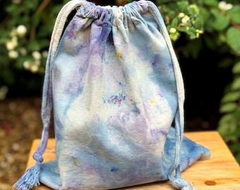 Könnte beinhalten: Eine blaue und weiße Batik-Kordeltasche mit weißen Kordeln. Die Tasche ist aus weichem, natürlichem Stoff gefertigt und hat einen entspannten, bohemian Stil.