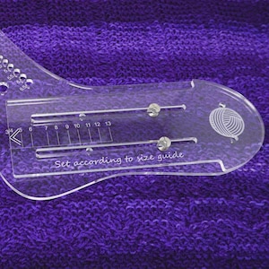 May include: A clear plastic knitting gauge with a yarn ball icon and a sliding scale marked with numbers 3, 4, 5, 6, 7, 8, 9, 10, 11, 12, and 13. The text "Set according to size guide" is printed on the gauge.
