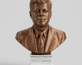 以下が含まれることがあります： ジョン・F・ケネディのブロンズ色の胸像。表情、髪、ネクタイ付きのスーツジャケットが詳細に表現されています。彫刻は白い斑点のある長方形の台座の上に設置されており、前面には「John F. Kennedy」という名前が刻まれています。