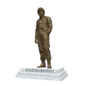 Puede incluir: Estatua de bronce de una persona con un traje de carreras, de pie con una mano en el bolsillo. La estatua está sobre una base de mármol con el nombre "JODY SCHECKTER". La figura tiene el pelo corto y lleva botas.