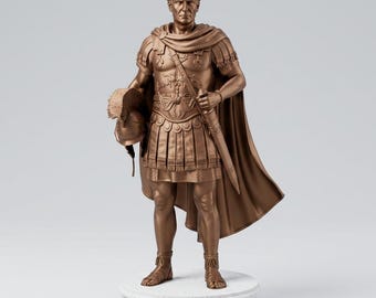 May include: A bronze-colored statue of Julius Caesar standing on a circular white base with the name JULIUS CAESAR printed on the front. The figure wears Roman military armor, a cloak, and sandals, while holding a helmet in the right hand.