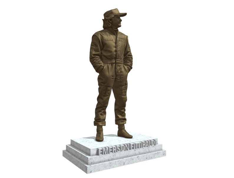 May include: A bronze-colored statue of a person in a racing suit and cap, standing on a marble base. The base is inscribed with the name "EMERSON FITTIPALDI". The statue has its hands in its pockets.