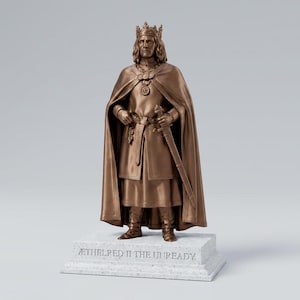 May include: A bronze-colored statue of a monarch wearing a crown, a long cloak, and a tunic, holding a sword at the waist. The figure stands on a rectangular stone-colored base with the engraved text AETHELRED II THE UNREADY.