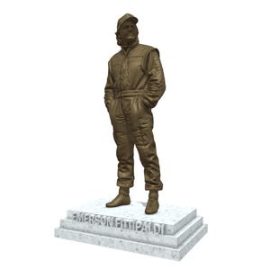 May include: A bronze statue of a person in a racing suit and cap, standing with hands in pockets. The statue is on a marble base with the name "EMERSON FITTIPALDI" inscribed. The figure is detailed, capturing the texture of the clothing.