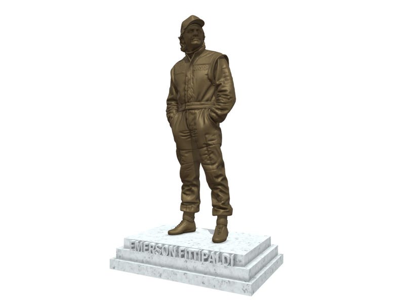May include: A bronze statue of a person in a racing suit and cap, standing with hands in pockets. The statue is on a marble base with the name "EMERSON FITTIPALDI" inscribed. The figure is detailed, capturing the texture of the clothing.