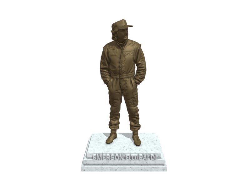 May include: A bronze-colored statue of a person in a racing suit and cap, standing with hands in pockets. The statue is mounted on a rectangular base with the name "EMERSON FITTIPALDI" engraved on it.