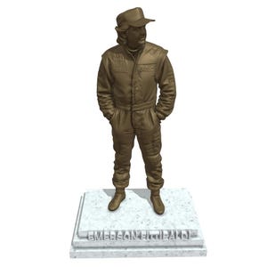 May include: A bronze-colored statue of a person in a racing suit and cap, standing with hands in pockets. The statue is on a rectangular base with the name "EMERSON FITTIPALDI" engraved on it.