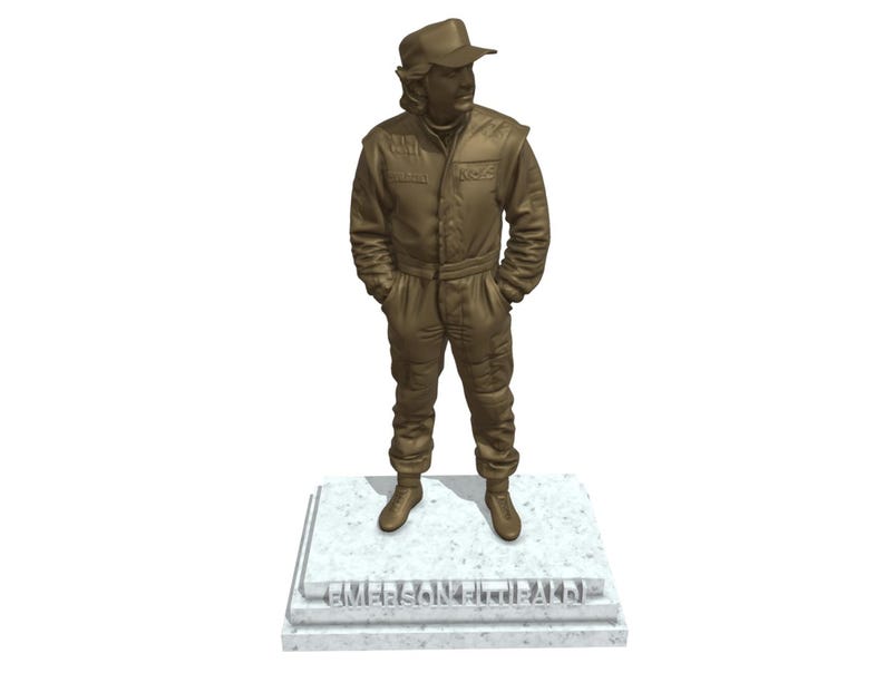 May include: A bronze-colored statue of a person in a racing suit and cap, standing with hands in pockets. The statue is on a rectangular base with the name "EMERSON FITTIPALDI" engraved on it.