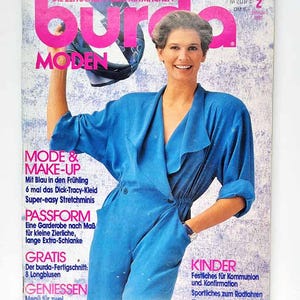 Może przedstawiać: Okładka magazynu w stylu vintage z kobietą w niebieskim kombinezonie. Tytuł "burda MODEN" jest w kolorze różowym. Tekst na okładce zawiera "MODE & MAKE-UP" i "KINDER". Okładka ma estetykę retro.