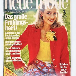 Puede incluir: Una portada de revista con una mujer que lleva una chaqueta roja, una blusa amarilla y una falda floral. La revista se titula "neue mode" y el texto de la portada dice "Das große Frühlings-heft!" y "Sportlich in den hochaktuellen Afrika-Farben!"