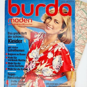 Op de afbeelding: Een vintage tijdschriftcover voor Burda Moden, met een vrouw in een rood-witte bloemenjurk. De titel van het tijdschrift is in rood-witte letters, en de tekst eronder luidt "Das große Heft der schönen Kleider" en "macht Mode zum Mitmachen".