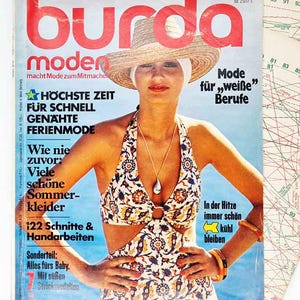 May include: A vintage Burda Moden magazine cover featuring a woman in a floral print halter top and straw hat. The cover has German text and a retro aesthetic, with sewing patterns in the background. The magazine is from 2017.