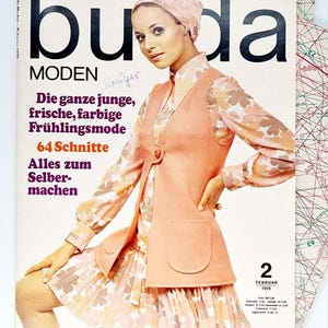Puede incluir: Una portada de revista vintage con una mujer que lleva un vestido floral rosa y blanco y un chaleco rosa. La revista se titula "buda MODEN" y el texto "Die ganze junge, frische, farbige Frühlingsmode 64 Schnitte Alles zum Selber-machen" está impreso en la portada. La fecha "2 FEBRUAR 1970" también está impresa en la portada.