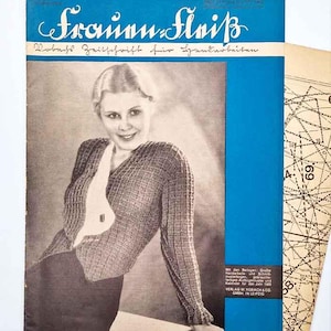 Puede incluir: Portada de revista vintage "Frauen Fleiß" en alemán, con una mujer con un suéter de punto. La portada es azul y la revista es de 1906. Se ve una hoja de patrones. El título de la revista está en escritura adornada.