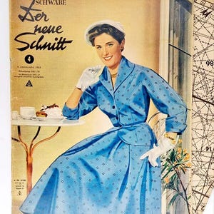 Pode incluir: Uma capa de revista vintage com uma mulher em um vestido azul com bolinhas brancas. A revista é intitulada "Der neue Schnitt" e tem o número 4 na capa. A mulher está sentada em uma mesa com um prato de comida e um copo de leite.