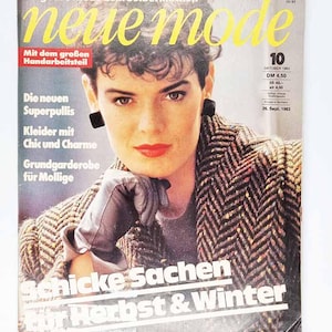 May include: A vintage fashion magazine cover with a woman in a patterned jacket and gloves. The magazine title is "neue mode" in yellow, with German text. The cover promotes sewing patterns and autumn/winter fashion. The issue is dated October 1983.