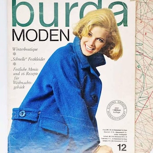 May include: A vintage Burda Moden magazine cover from December 1964. The cover shows a smiling woman in a bright blue coat. The magazine title is in large green letters. Text includes "Winterboutique" and "Festliche Menüs".