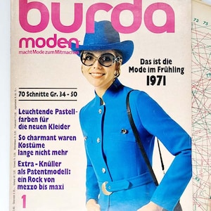Peut inclure: Une couverture vintage du magazine Burda Moden de janvier 1971. La couverture présente une femme vêtue d'une tenue et d'un chapeau bleus, avec de grandes lunettes. Le titre du magazine est en rose, avec du texte en allemand. Le texte "70 Schnitte Gr. 34-50" est également présent.