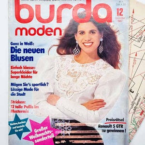 May include: A vintage magazine cover featuring a woman in a white blouse with lace detailing. The magazine title "Burda Moden" is in large red letters. Text includes "Die neuen Blusen" and "Großer Weihnachts-sonderteil".