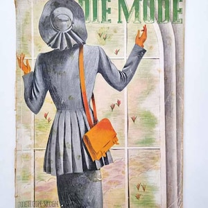 Op de afbeelding: Omslag van een vintage tijdschrift met een vrouw in een grijs pak en hoed, van achteren gezien, met een oranje handtas. De vrouw staat voor een raam. De tijdschrifttitel "DIE MODE" staat in groene letters bovenaan.