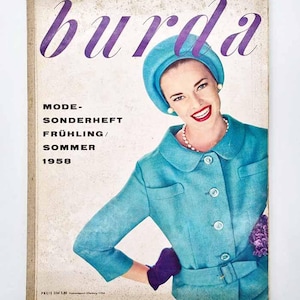 Op de afbeelding: Vintage magazinecover met een vrouw in een turquoise pak en hoed, parelketting en paarse handschoenen. De tijdschrifttitel "burda" staat in paars schrift. Tekst bevat "MODE-SONDERHEFT FRÜHLING/SOMMER 1958". De cover heeft een versleten, verouderde uitstraling.