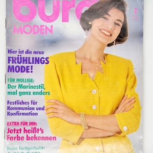 May include: A magazine cover featuring a woman wearing a yellow jacket and a plaid skirt. The magazine is titled "Burda MODEN" and the text "Hier ist die neue FRÜHLINGS MODE!" is visible.
