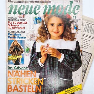 May include: A vintage November 1988 issue of the German magazine Neue Mode featuring a cover image of a child with curly brown hair wearing a dark green and blue plaid dress with a white collar, surrounded by text and small graphic inserts.