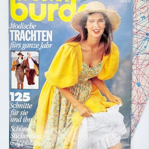 May include: A magazine cover featuring a woman wearing a yellow dress and a straw hat. The magazine is titled "Special Burda" and features the text "Modische Trachten fürs ganze Jahr" and "125 Schnitte für sie und ihn Schöne Stickereien & Applikationen".