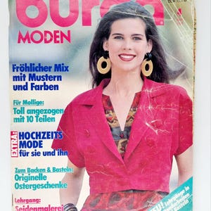 Puede incluir: Una portada de revista con una mujer que lleva una chaqueta rosa con una camisa estampada de colores debajo. La revista se titula "Burda MODEN" y tiene el texto "Fröhlicher Mix mit Mustern und Farben" y "EXTRA: HOCHZEITS MODE für sie und ihn".