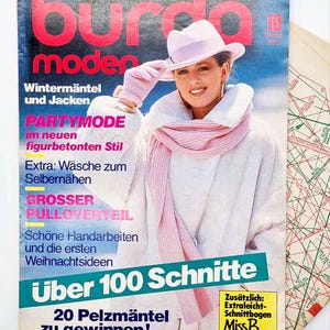 May include: A retro magazine cover with a woman wearing a pink hat, scarf, and coat. The magazine is titled "Burda Moden" in pink. Text includes "Winter Coats and Jackets" and "Over 100 Patterns".