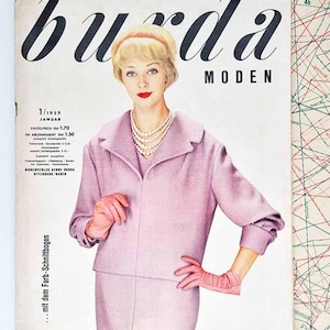 Könnte beinhalten: Titelseite des Burda Moden Magazins vom Januar 1959. Das Cover zeigt eine Frau in einem rosa Kostüm, Handschuhen und einer Perlenkette. Der Magazintitel ist in großer schwarzer Schrift. Der Text ist auf Deutsch.