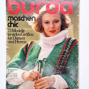 May include: A vintage Burda magazine cover titled Maschen chic featuring 73 Modelle in vielen Größen für Damen und Herren. The cover displays a person wearing a white turtleneck sweater under a green knitted cardigan with red and black trim.