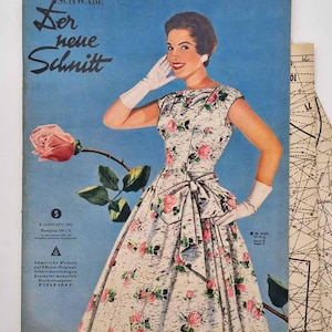 Op de afbeelding: Vintage mode tijdschriftcover met een vrouw in een bloemenjurk en strik. De cover heeft de tekst "Der neue Schnitt" en een roze roos. De achtergrond is lichtblauw.