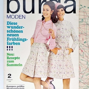 Könnte beinhalten: Ein Vintage-Magazincover mit zwei Frauen in Blümchenkleidern. Das Magazin heißt "Burda MODEN" und der Text "Diese wunder-schönen neuen Frühlings-farben!!! Neu: Rezepte zum Sammeln 2 FEBRUAR 1968 Europas größte Modenzeitschrift" ist auf dem Cover gedruckt.