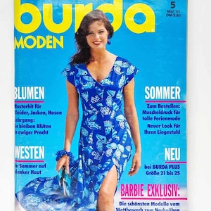Puede incluir: Una portada de revista vintage con una mujer con un vestido azul estampado. El título de la revista es "burda MODEN" con texto en alemán. El texto adicional incluye "BLUMEN" y "SOMMER". La portada tiene un fondo azul.