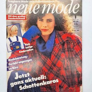 Puede incluir: Una portada de revista vintage con una mujer con una chaqueta a cuadros roja y negra y una bufanda azul. El título de la revista es "neue mode". El texto en alemán incluye "Mit dem großen Handarbeitsteil" y "Jetzt ganz aktuell: Schottenkaros".