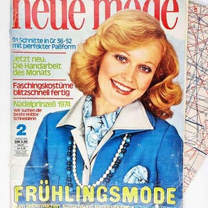 Könnte beinhalten: Ein Vintage-Magazin-Cover mit einer lächelnden Frau mit blonden Haaren. Das Cover trägt den Titel "neue mode" in Rot, mit Text auf Deutsch. Die Frau trägt eine blaue Jacke und einen Schal mit floralem Muster. Das Magazin ist von 1974.