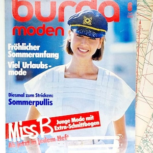 May include: A vintage magazine cover with a woman in a navy captain's hat with gold trim. The magazine title "burda moden" is in red. Text includes "Sommerpullis" and "Miss B". The cover is from June 1984.