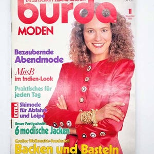 Può includere: Una copertina di rivista con una donna in giacca rossa e gioielli dorati. Il titolo della rivista "Burda Moden" è in rosso. Il testo include "Bezaubernde Abendmode" e "Backen und Basteln". La copertina è del novembre 1989.