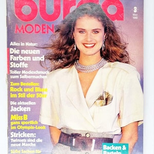 May include: Cover of "Burda Moden" magazine, featuring a woman with long brown hair, wearing a white blouse and a silver necklace. The magazine title is in large red letters. Text includes "Die neuen Farben und Stoffe" and "Backen & Basteln zu Ostern."