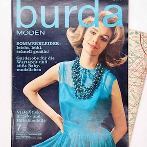 May include: A vintage Burda Moden magazine cover from July 1963 featuring a person wearing a bright blue sleeveless dress and a multi-strand beaded necklace. The cover text includes 'burda MODEN', 'SOMMERKLEIDER', and 'Viele Stick-, Strick- und Häkelmodelle'.