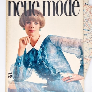 May include: A vintage magazine cover featuring a woman wearing a blue paisley patterned blouse with a white collar and a white hat. The magazine is titled "neue mode" and the date is May 1966. The text "Neuer Schnitt" is at the bottom of the cover.