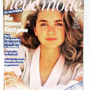 Può includere: Una copertina di rivista vintage con il ritratto di una donna. Il titolo "neue mode" è in rosa. Il testo include "Die neuen Kostume" e "Für den Frühling". La copertina ha un'estetica retrò, incentrata sulla moda.