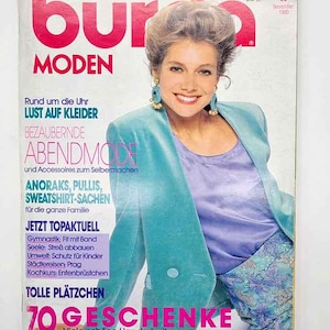 May include: A vintage magazine cover featuring a woman in a teal blazer and a purple top. The magazine title is "Burda Moden" in large pink letters. Text includes "Evening Fashion" and "70 Gifts".