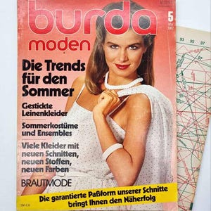 Op de afbeelding: Een vintage Burda Moden magazine cover uit mei 1982, met een vrouw in een witte polkadotjurk. De cover heeft Duitse tekst, waaronder "Die Trends für den Sommer" en "BRAUTMODE". Een patroonvel is zichtbaar.