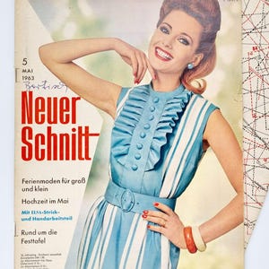 Könnte beinhalten: Ein Vintage-Magazincover mit einer Frau in einem blau-weiß gestreiften Kleid mit Rüschenkragen. Das Magazin heißt "Neuer Schnitt" und der Covertext lautet "Ferienmoden für groß und klein, Hochzeit im Mai, Mit ELSA-Strick- und Handarbeitsteil, Rund um die Festtafel".