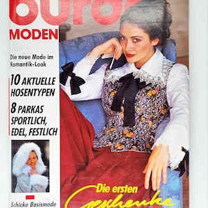 May include: A vintage magazine cover featuring a woman in a floral vest, white shirt, and red pants. The magazine title is "Burda Moden" with text in German. The cover includes text about fashion trends and the October '93 issue.