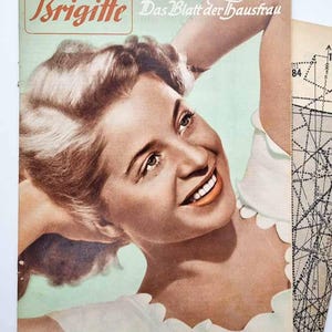 Puede incluir: Portada de revista vintage "Brigitte" con una mujer sonriente. El título es rojo y naranja. La portada incluye texto en alemán y una hoja de patrones. De mediados del siglo XX.